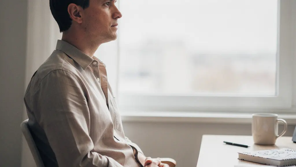 Une personne assise près d’une fenêtre, l’air pensif, dans un espace de travail sobre, avec une grande zone vide dans l’image pour suggérer une recherche de direction professionnelle.